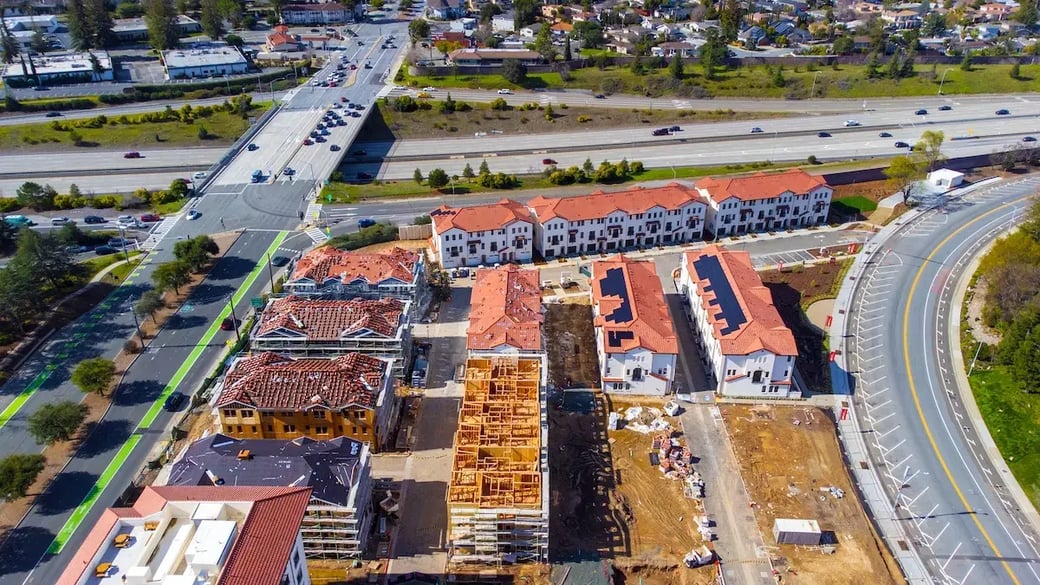 Aerial view of suburban housing development under construction near highway and residential neighborhoods.