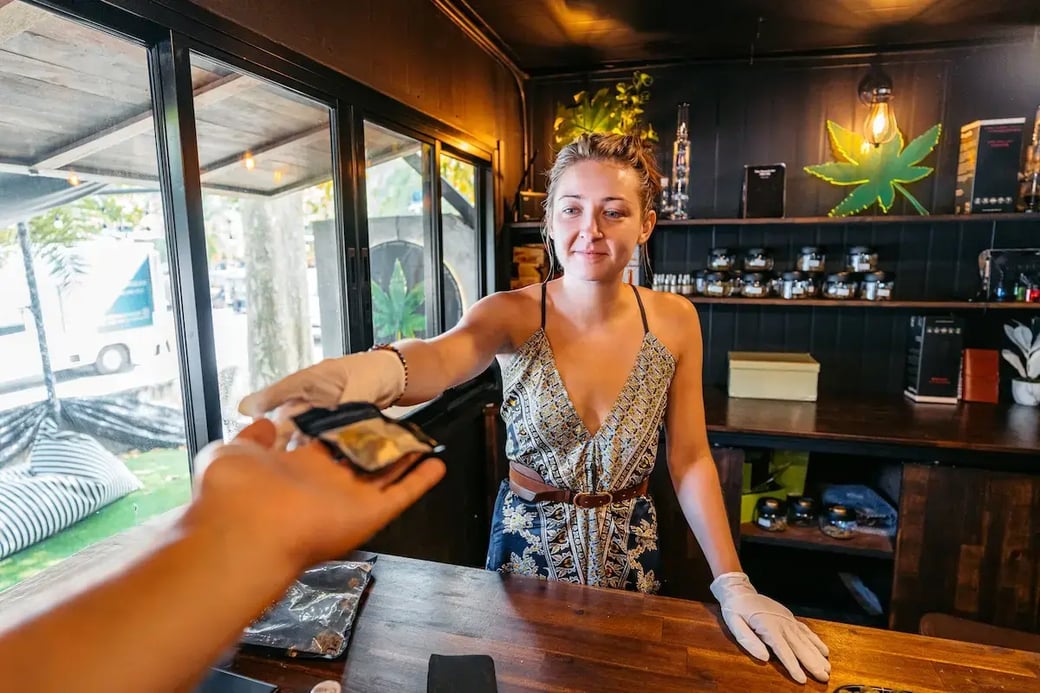 Female dispensary worker handing cannabis product to customer inside a licensed cannabis retail store.