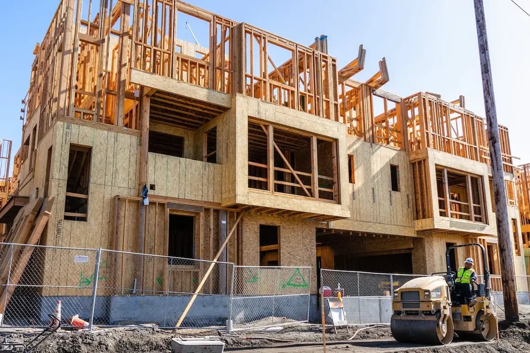 Framed multi-family housing development under construction with worker operating compactor on job site.