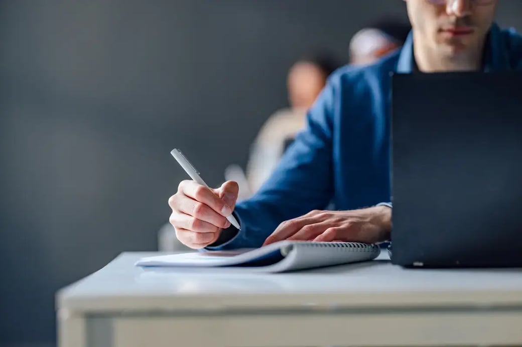 Man in suit taking notes while using a laptop.