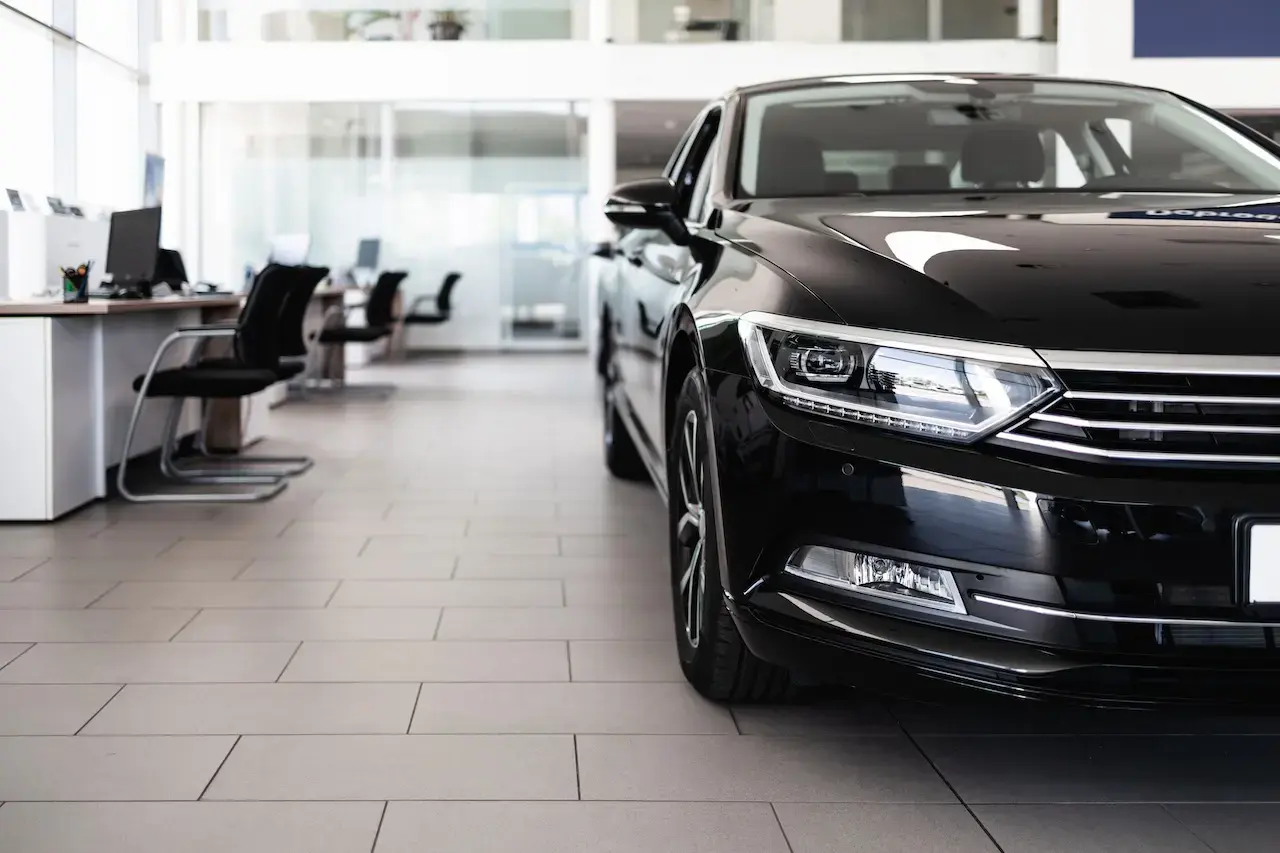 Close-up of black sedan in a modern auto dealership showroom with empty desks in the background