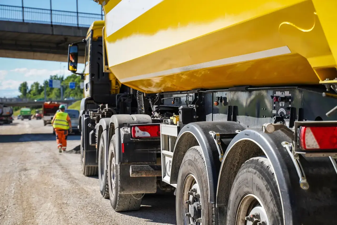 Yellow dump truck on a construction site with roadwork in progress and workers in high-visibility gear