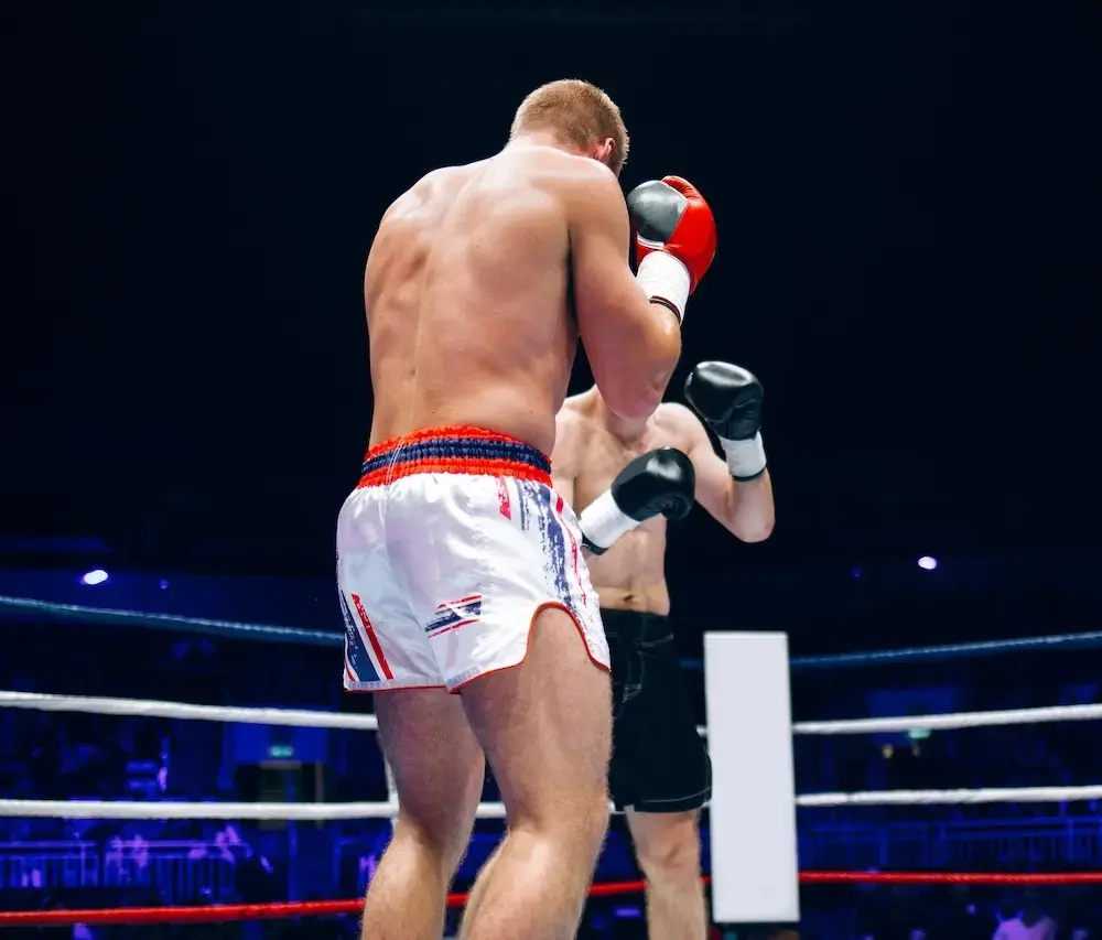 Professional boxers in the ring during a competitive match, athlete wearing UK flag trunks throws a punch at opponent