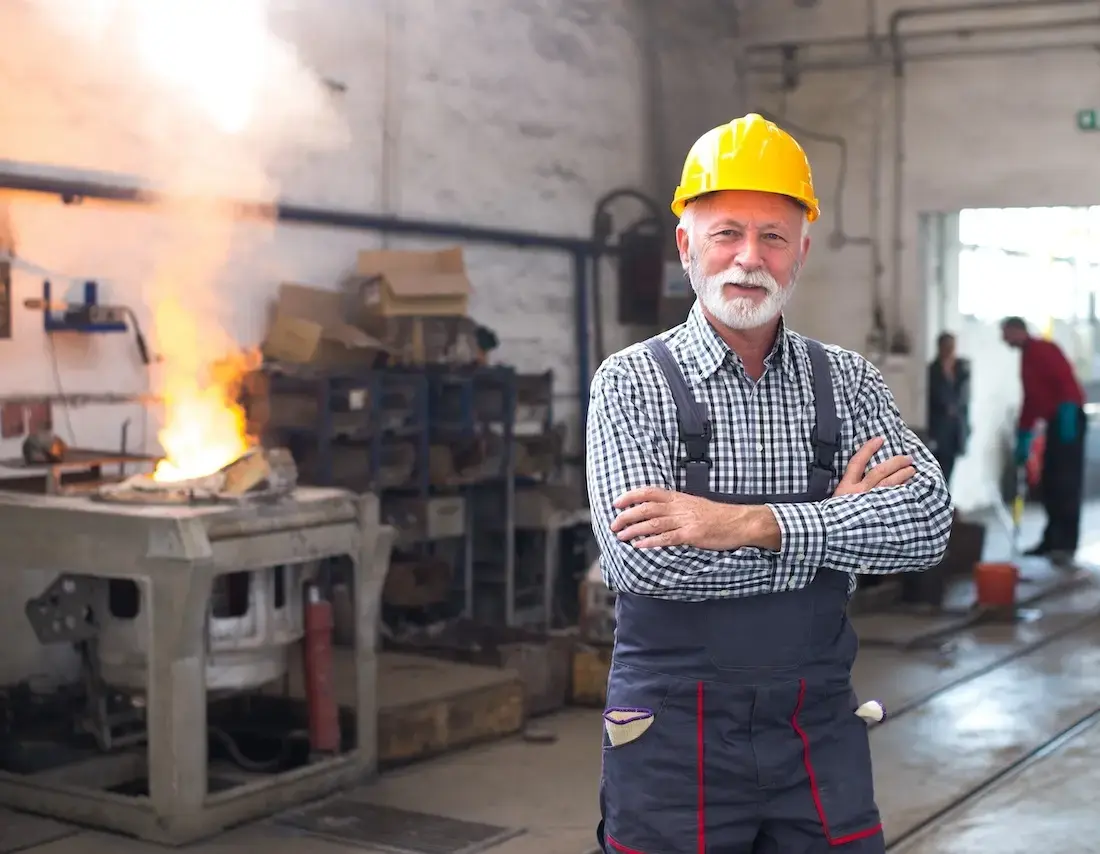 Senior construction worker in safety gear standing confidently in front of active foundry