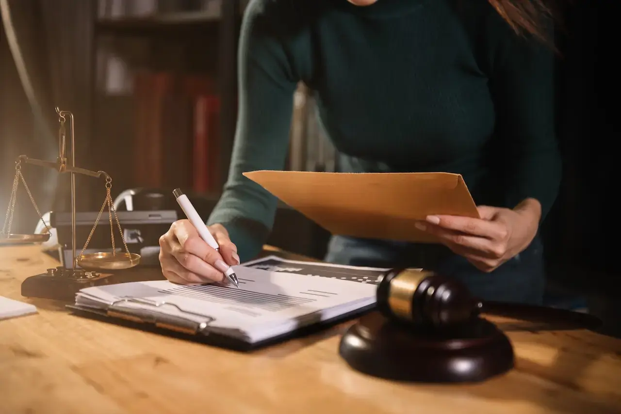 Woman signing legal court bond documents at a law office desk with a gavel and justice scale in view