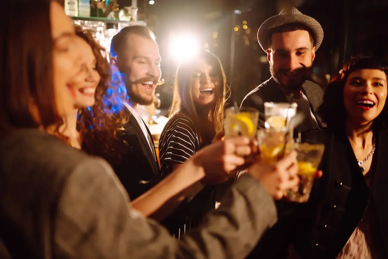Group of young adults cheering with cocktails at night in lively bar or restaurant setting